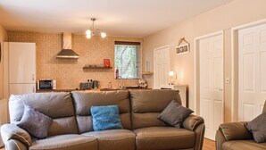 A living room with a brown leather sofa, a white coffee table, and a kitchen area with a microwave, toaster, and kettle. - 2 bedroom accommodation in Walwen, Lixwm (Walwen, Lixwm)