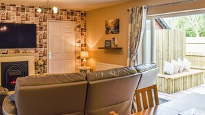 A cozy living room with a sofa, a fireplace, a television, and a window with a view of the outside. - 2 bedroom accommodation in Walwen, Lixwm (Walwen, Lixwm)