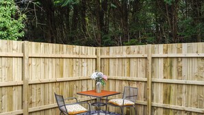 A patio with a wooden fence, two chairs, a table, and a vase with flowers. - 2 bedroom accommodation in Walwen, Lixwm (Walwen, Lixwm)