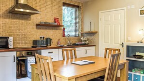 A compact kitchen with a microwave, toaster, and oven. There is a dining table with chairs and a window with blinds. - 2 bedroom accommodation in Walwen, Lixwm (Walwen, Lixwm)