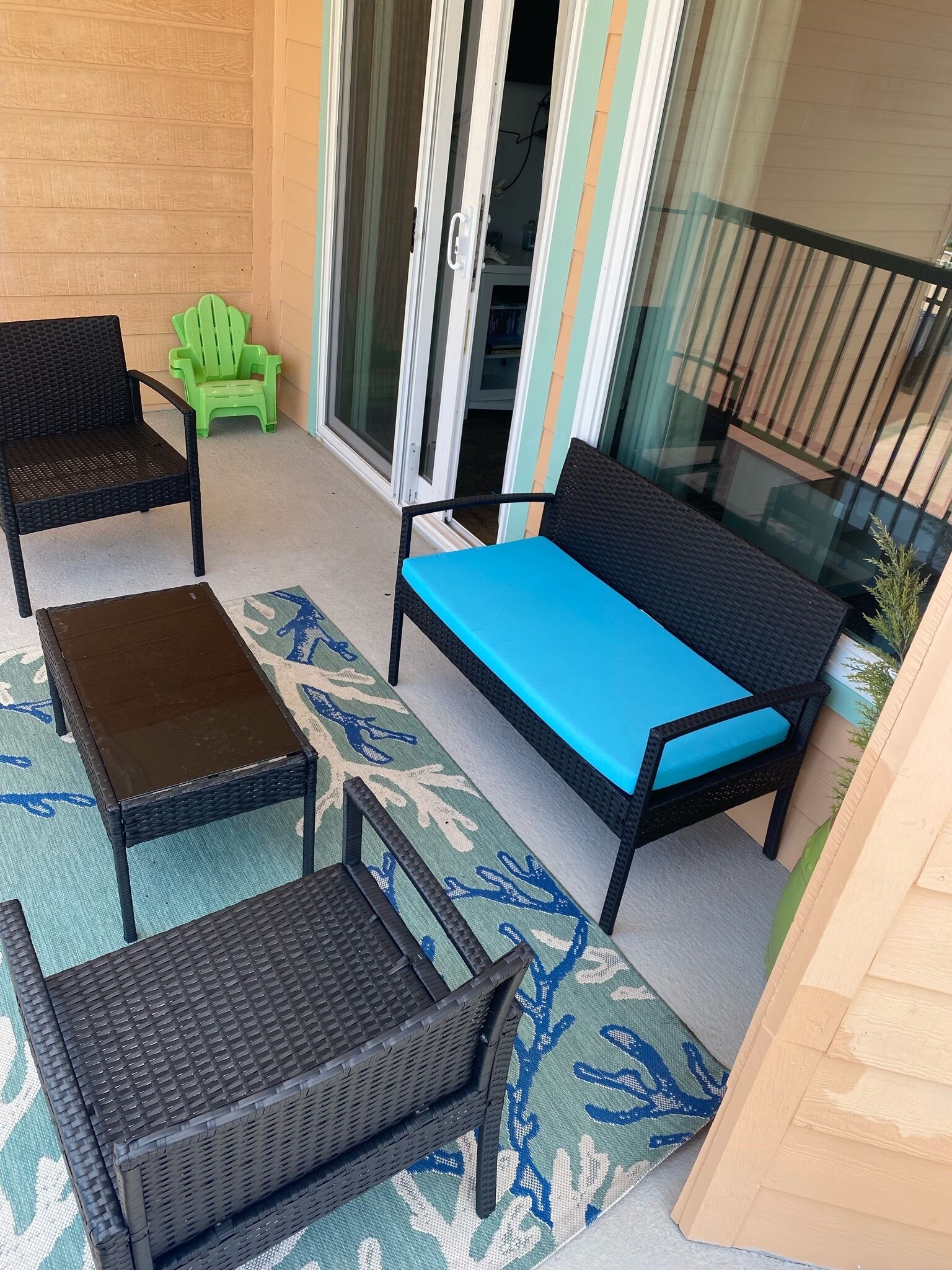A balcony with wicker furniture, a green chair, and a glass door leading to an interior space.