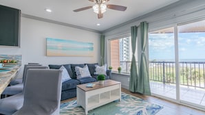 Ein Wohnzimmer mit einer Couch, einem Couchtisch, einem Deckenventilator und einem großen Fenster mit Blick auf den Strand.