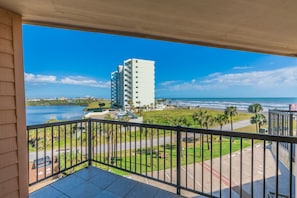 Un balcon avec vue sur une plage, un parking et un immeuble de grande hauteur.