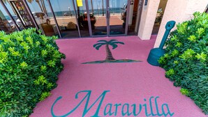 Un viale rosa con la scritta 'Maravilla' e un simbolo di palma che conduce all'ingresso di un edificio.