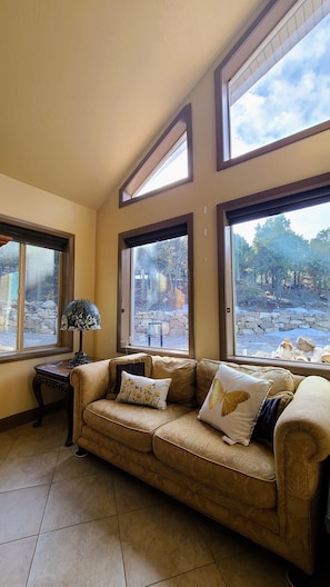 Relax in this inviting living room with a sofa, table, and large windows offering a view of the surrounding landscape.