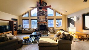 A spacious living room with a stone fireplace, large windows, and a ceiling fan. - Private and secluded mountain cabin (Cedar City)