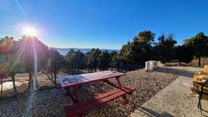 A picnic table with a metal container, surrounded by pebbles and trees, with a clear view of distant mountains under a bright sun. - Private and secluded mountain cabin (Cedar City)