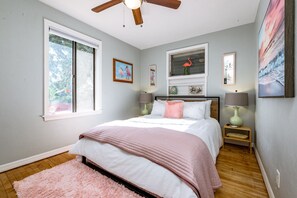 Quarto com cama, duas mesas de cabeceira com abajures, ventoinha no teto e obras de arte nas paredes.