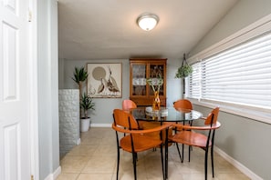 Uma área de refeições com uma mesa de vidro redonda, quatro cadeiras de madeira, um armário com portas de vidro e uma planta em vaso.