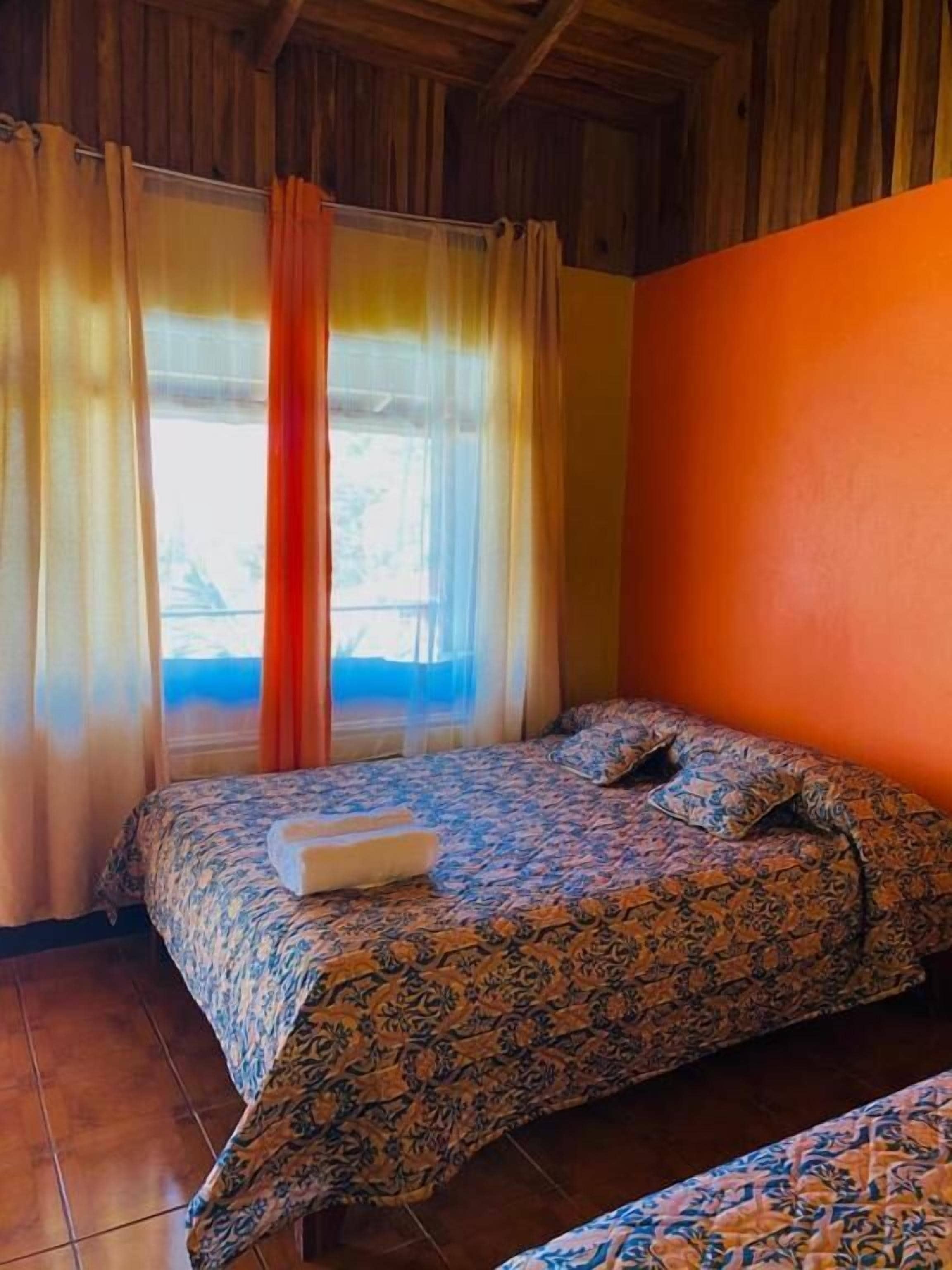 A room with a bed, a window with curtains, and a wooden ceiling.