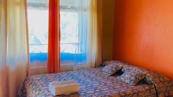 A room with a bed, a window with curtains, and a wooden ceiling.