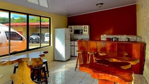 A kitchen with a red wall, a white refrigerator, and a wooden bar counter with stools. - El Nido Lodge (Monteverde)