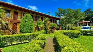 A building with a pathway leading to the entrance, surrounded by well-maintained greenery and a clear blue sky. - El Nido Lodge (Monteverde)