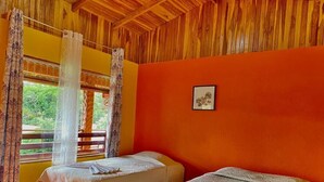 A room with two beds, wooden ceiling, orange walls, and a window with curtains. - El Nido Lodge (Monteverde)
