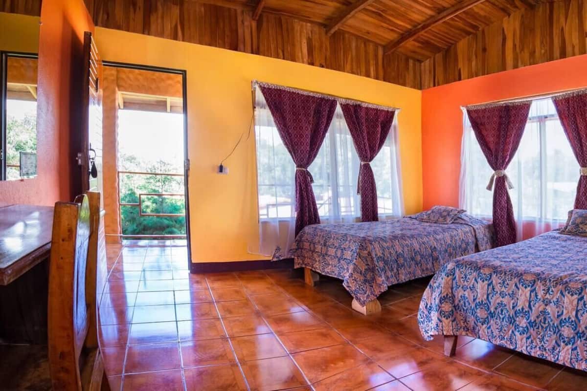 A room with two beds, wooden ceiling, orange walls, and a tiled floor.