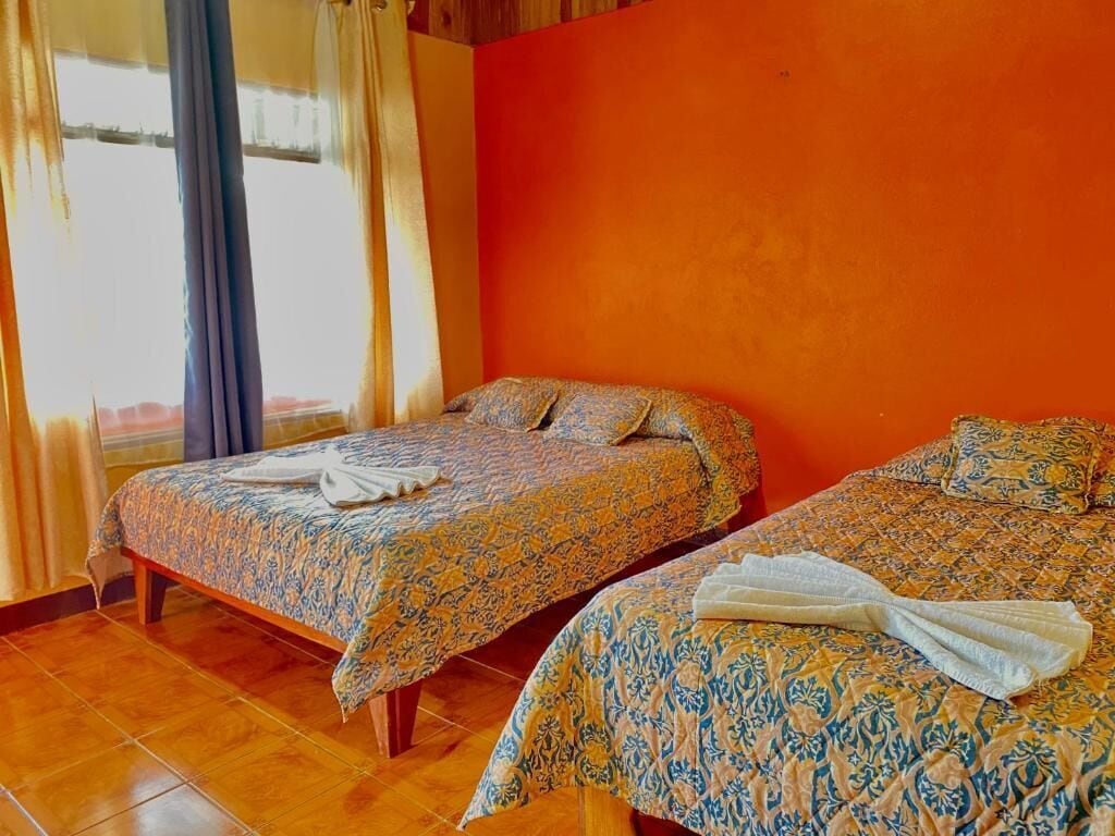 Two beds with patterned bedding, a window with curtains, and a tiled floor.