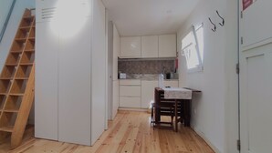 Una cocina compacta con armarios blancos, una escalera de madera y un pequeño comedor con mesa y sillas.
