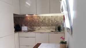 Una cocina compacta con armarios blancos, un salpicadero con diseño, una mesa de comedor de madera y una pequeña planta en maceta.