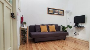 Una sala de estar moderna con un sofá de color oscuro, un televisor de pantalla plana y piso de madera.