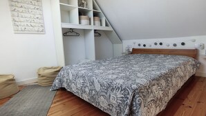 Un dormitorio con cama, suelo de madera, lámpara colgante y pared blanca con una obra de arte de un pájaro.