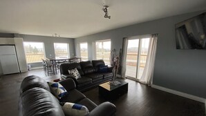 A spacious living room with a dark leather couch, a coffee table, and a dining area with a table and chairs. - Red Roof Chalet in close proximity to beaches, trails, golf and Blue Mountains. (Meaford)