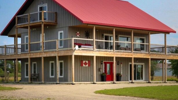 A two-story building with a red roof and a balcony on the upper floor. - Red Roof Chalet in close proximity to beaches, trails, golf and Blue Mountains. (Meaford)