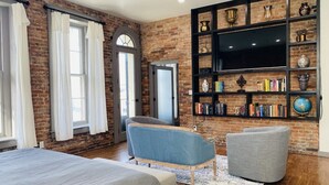 A modern living room with a brick wall, a bookshelf, and a large TV. - 4 Bed, 3 Bath Loft in Downtown Louisville! Amazing River Views! Private Deck! (Louisville)