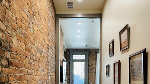A hallway with a brick wall on one side and a wooden floor, leading to a room with a door and a window. - 4 Bed, 3 Bath Loft in Downtown Louisville! Amazing River Views! Private Deck! (Louisville)