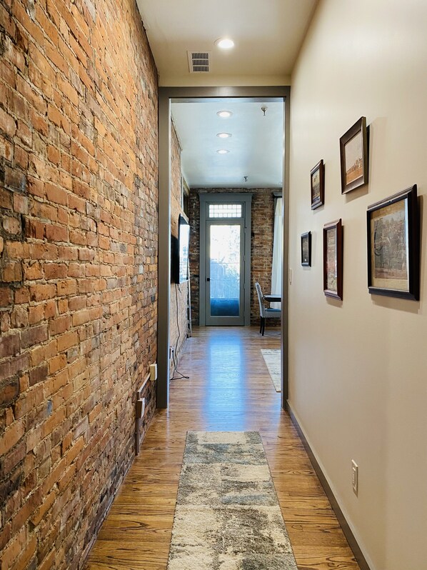 A hallway with a brick wall on one side and a wooden floor, leading to a room with a door and a window. - 4 Bed, 3 Bath Loft in Downtown Louisville! Amazing River Views! Private Deck! (Louisville)