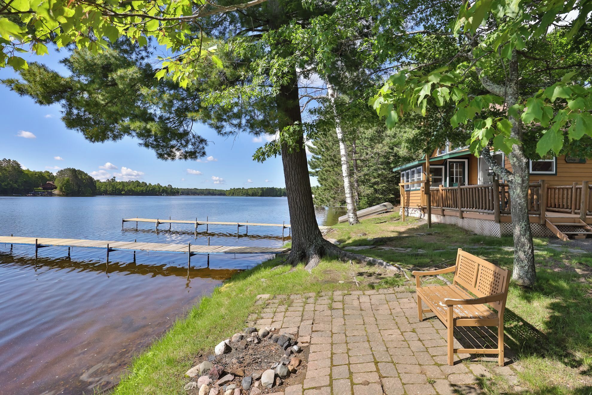 A lakeside cabin with a dock, a wooden bench, and a fire pit.