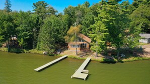 A cabin surrounded by dense forest, with a dock extending into a calm lake.