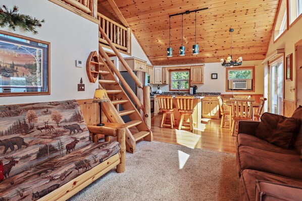 A wooden interior with a sofa, a brown couch, a staircase, and a kitchen area.
