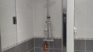 A shower with a handheld showerhead and a wall-mounted faucet, a small shelf with a bottle, and a door with a handle. - Comfortable apartment with garden access and weights room (Mardié)