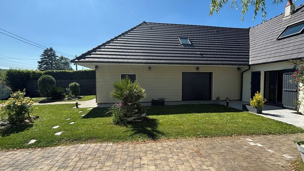 A two-story house with a dark roof, a garage, and a well-maintained lawn. - Comfortable apartment with garden access and weights room (Mardié)