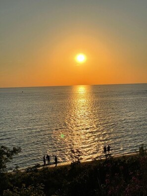 Um pôr do sol sobre um mar calmo, com algumas pessoas na praia.