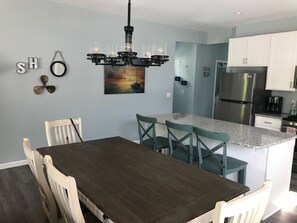 Uma cozinha moderna com ilha central, armários brancos e uma geladeira de aço inoxidável.