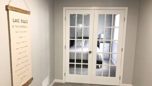 A room with a white door, a framed sign on the wall, and a bed with a white headboard.