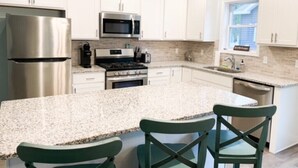 A kitchen with white cabinets, stainless steel appliances, a granite countertop, and green chairs.