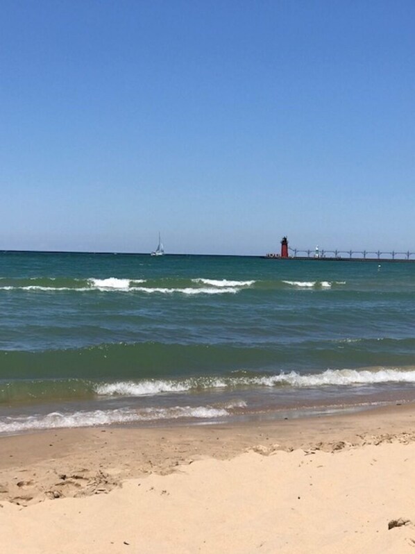 Uma praia com um cais que se estende para a água, um farol e um veleiro.