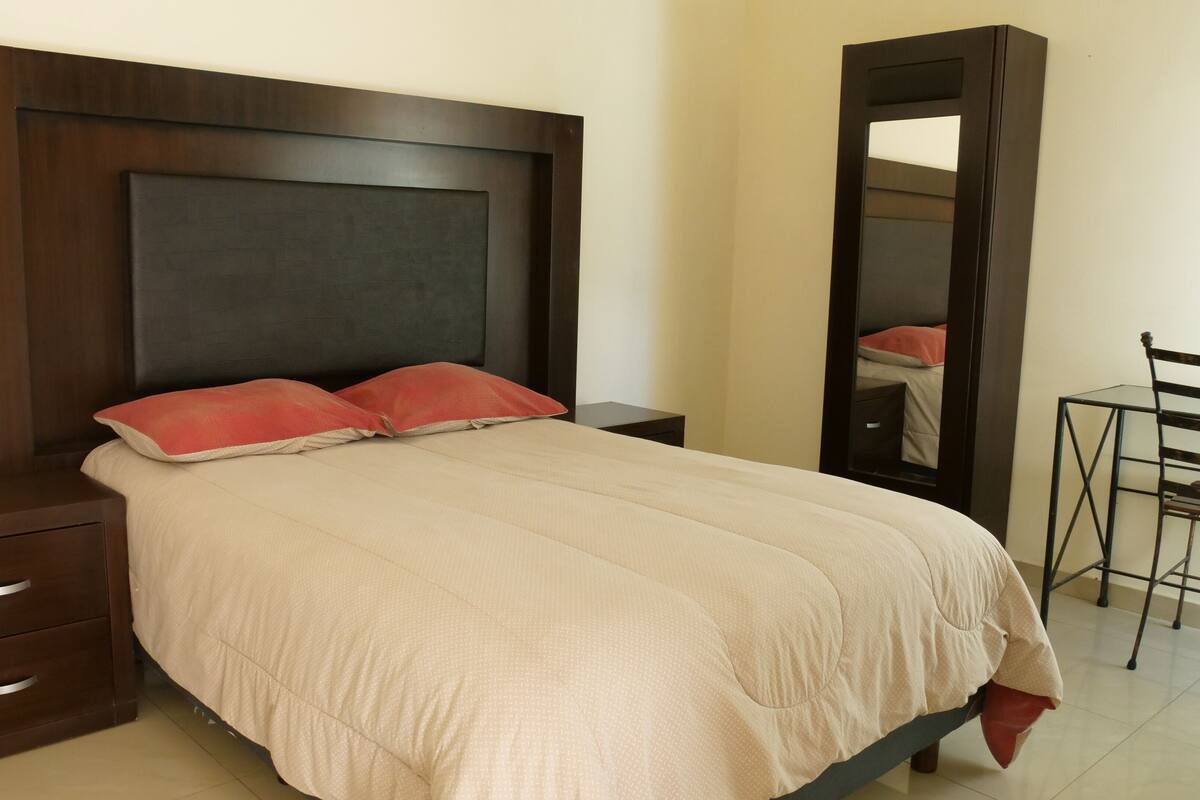 A neatly made bed with a headboard, two bedside tables, a mirror, and a chair.