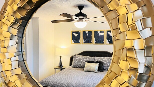 A bedroom with a bed, a ceiling fan, and a wall-mounted mirror with a golden frame.