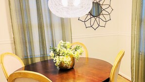 A dining area with a round wooden table, four chairs, a vase of flowers, and a wall-mounted decorative piece.