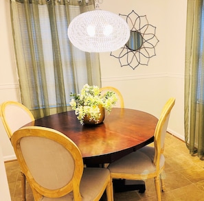 A dining area with a round wooden table, four chairs, a vase of flowers, and a wall-mounted decorative piece. - Southern Charm-Convenient to Everything! (Lynchburg)