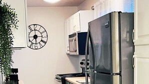 A kitchen with a stainless steel refrigerator, a microwave, and a clock on the wall.
