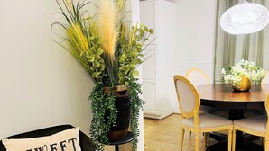 A cozy living room with a green sofa, a decorative plant stand, and a dining area with a wooden table and chairs.