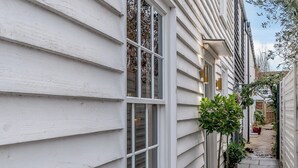 A narrow pathway flanked by white siding houses with windows and potted plants. - Anchor Light Cottage (Faversham)