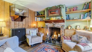 A cozy living room with a fireplace, wooden walls, and a bookshelf filled with books. - Anchor Light Cottage (Faversham)