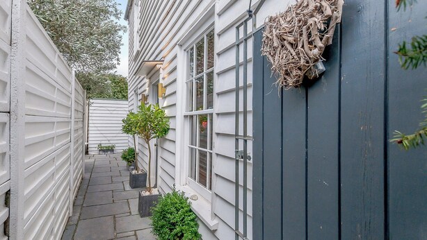 A narrow pathway flanked by white siding and a dark blue wall with a nest attached. - Anchor Light Cottage (Faversham)