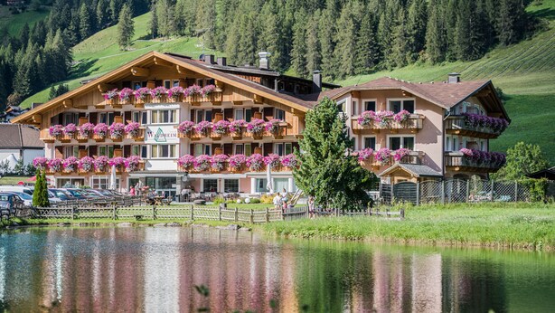 Un hôtel doté de nombreux balcons ornés de fleurs, avec un lac au premier plan et une chaîne de montagnes en arrière-plan.