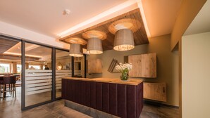 Un espace d’accueil moderne avec un comptoir de réception en bois, de grandes suspensions et une vue sur la salle à manger.